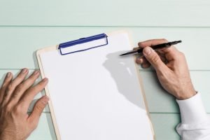 Una mano sostiene un bolígrafo sobre una tablilla con papel